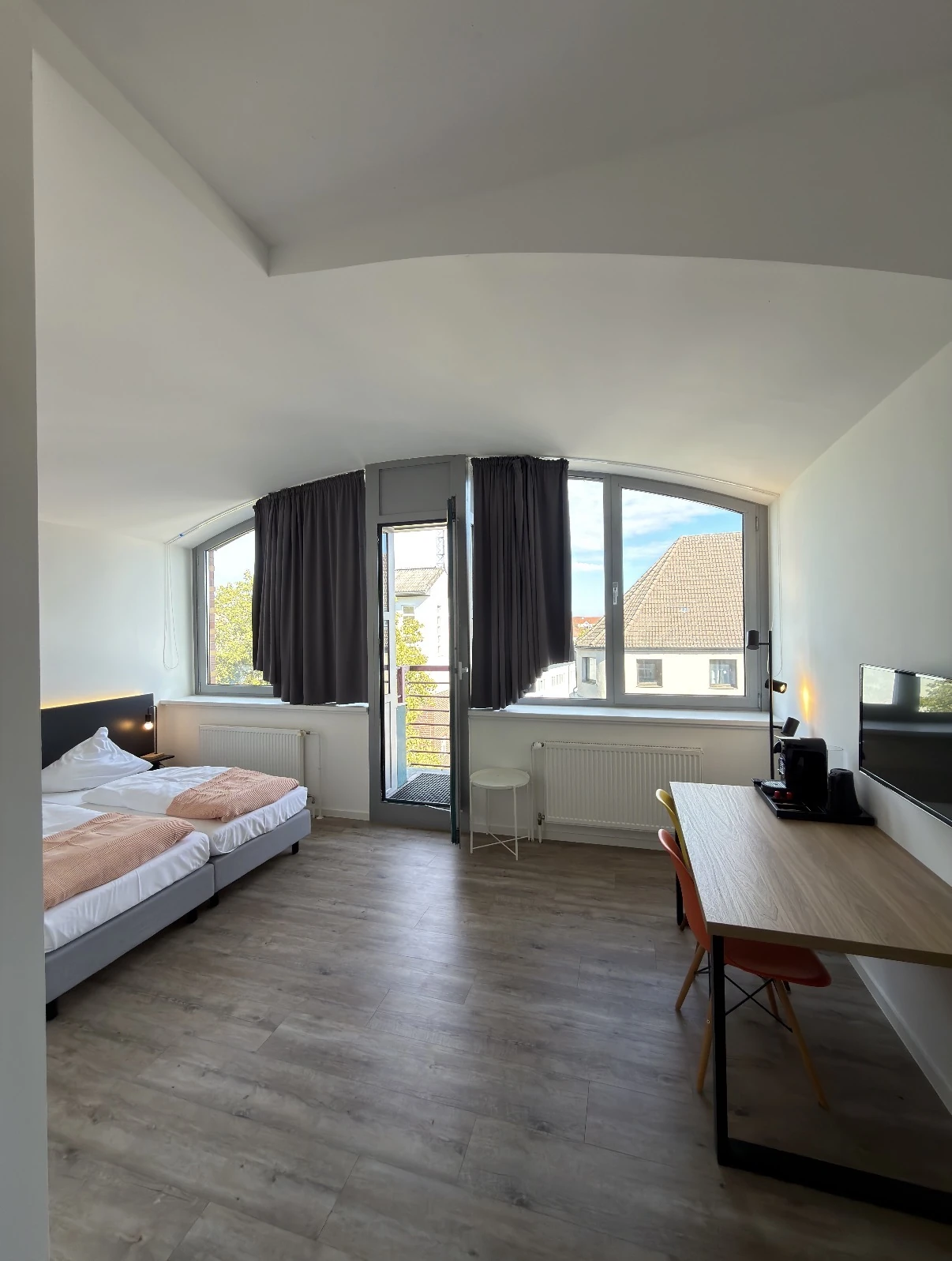 Helles Zimmer mit zwei Betten, Schreibtisch und geöffnetem Balkon