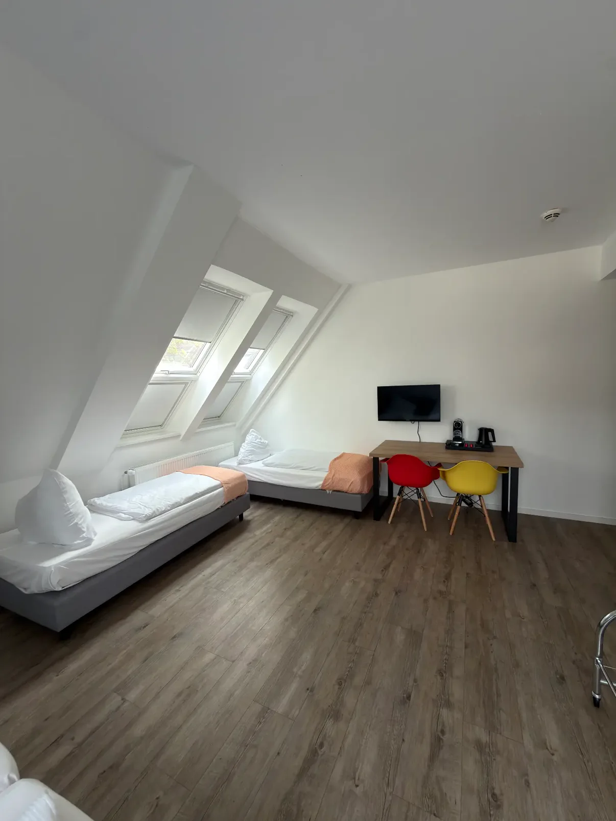 Geräumiges Dachzimmer mit zwei Einzelbetten und farbigen Stühlen am Tisch