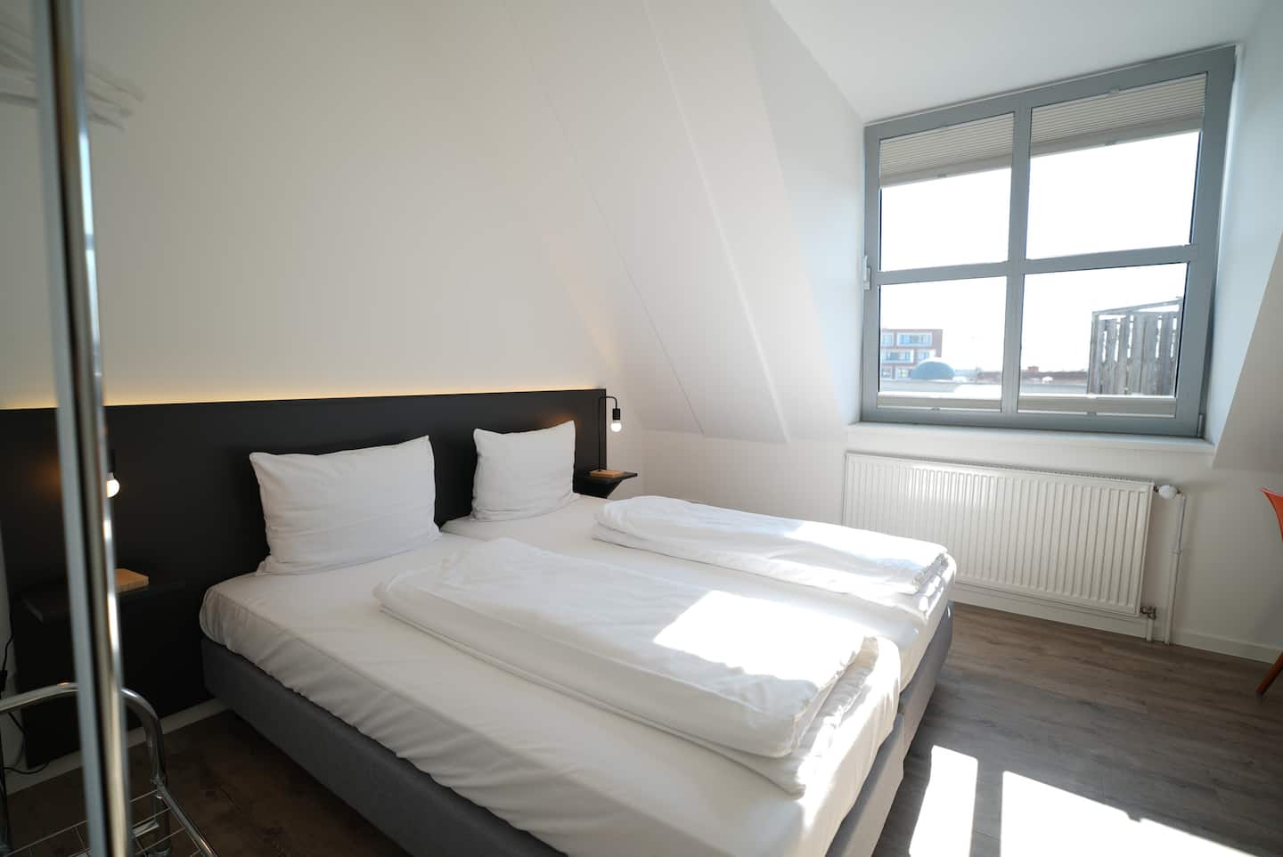 Doppelbett mit dunklem Kopfteil und Fenster daneben