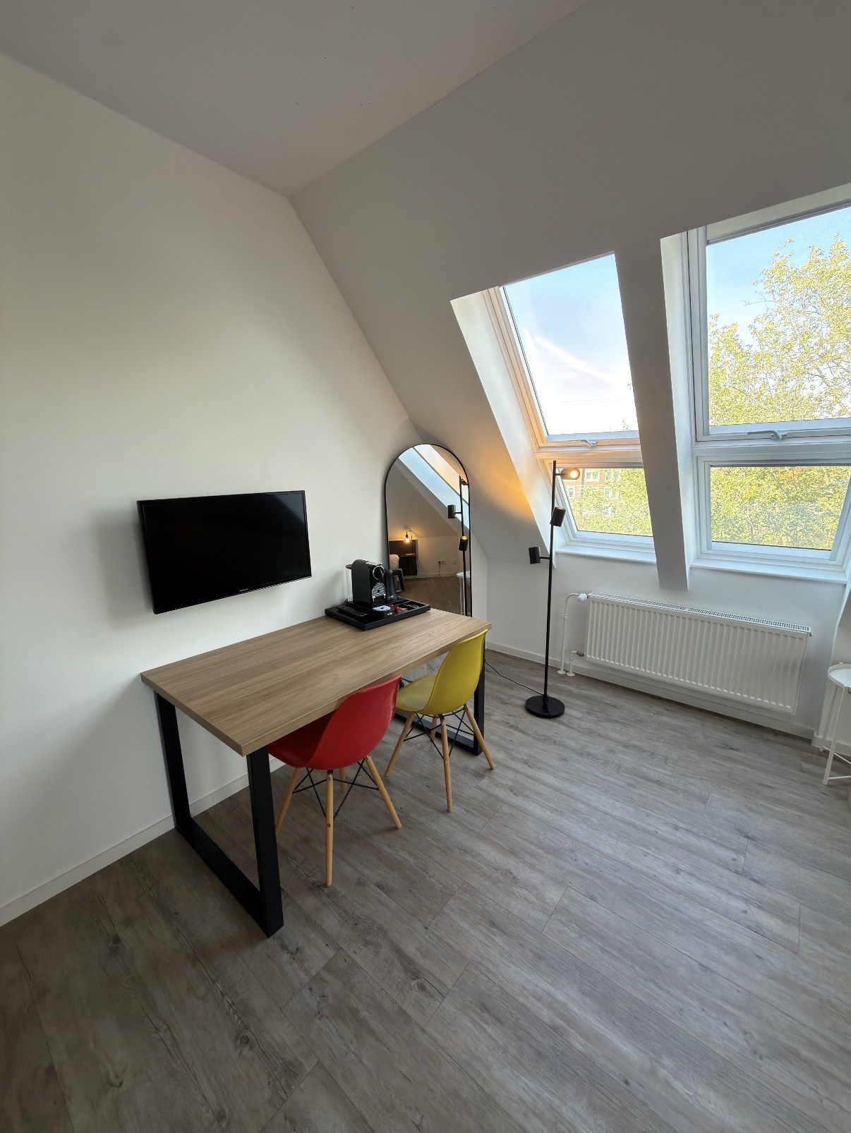 Arbeitstisch mit Kaffeemaschine, Flachbild-TV und Stehlampe am Fenster
