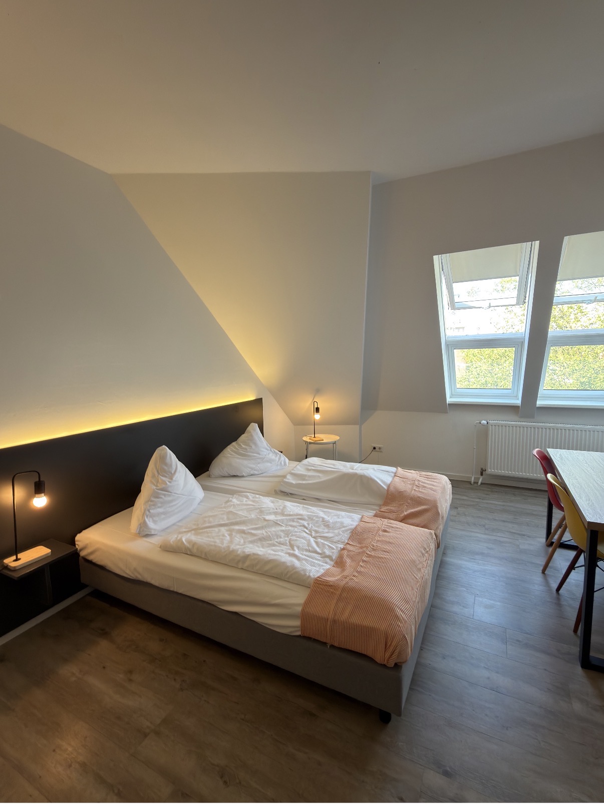 Doppelbett mit weißer Bettwäsche und indirekter Beleuchtung am Kopfende